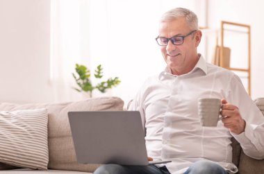 Elderly Man Using Laptop And Having Coffee