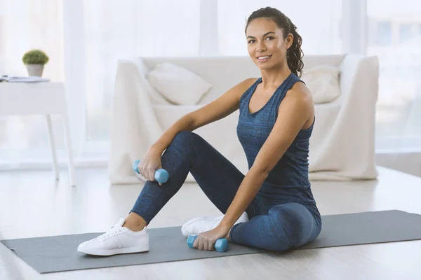Fit Hispanic woman with dumbbells resting after her training at home