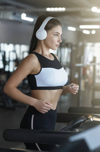 Sports and workout. Young woman with headphones using treadmill in gym — Stock Photo, Image