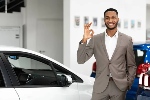 Mosolygós ügynök Gesturing Okay Standing In Luxury Auto Store — Stock Fotó