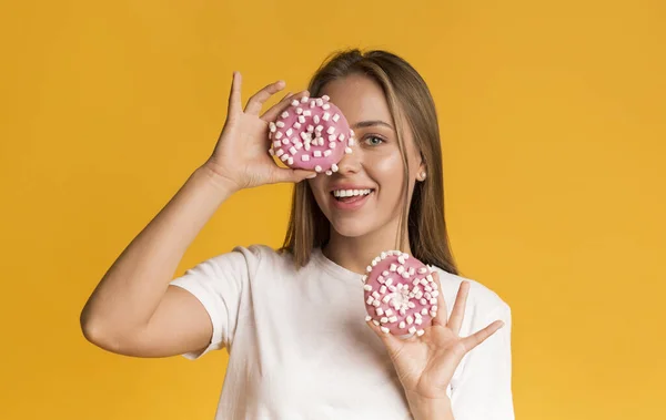 Engraçado mulher positiva segurando donuts perto de seu rosto e sinceramente sorrindo — Fotografia de Stock