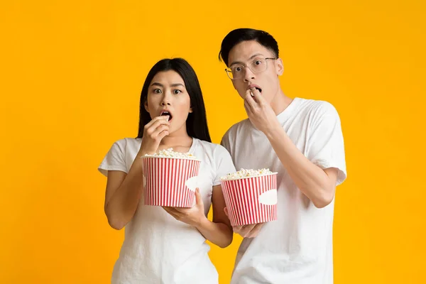 Shocked asian guy and girl eating popcorn, watching movie — Zdjęcie stockowe