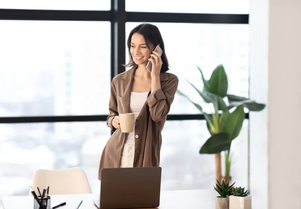 Chica hablando en el teléfono celular en la oficina sosteniendo taza — Foto de Stock