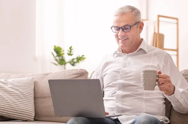 Homem idoso usando laptop e tomando café — Fotografia de Stock