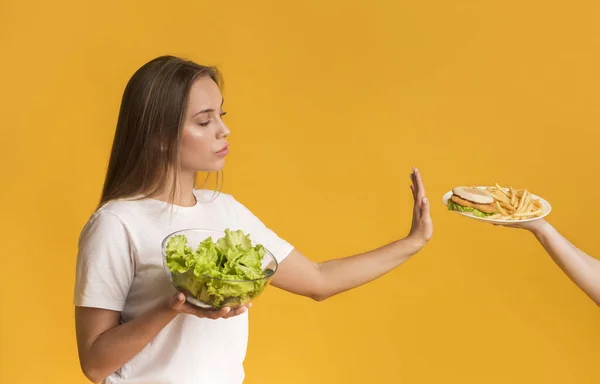 Confident young woman refusing plate with junk food and choosing salad — Zdjęcie stockowe