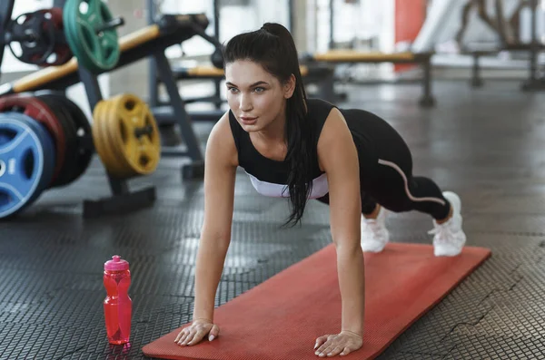 Young woman doing push ups on yoga mat in sports club — Stockfoto