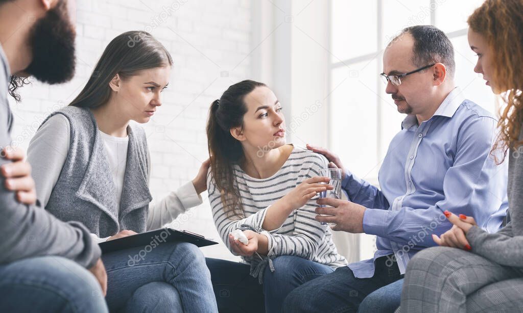Concerned support group mebers comforting emotional young woman at therapy session