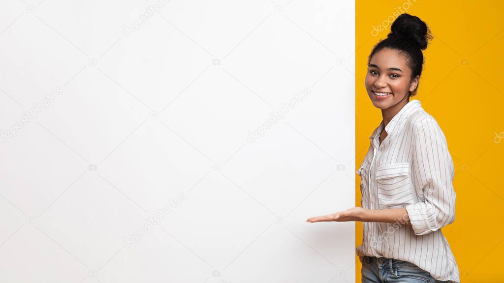 Cheerful Black Girl Pointing At White Advertisement Board With Open Hand