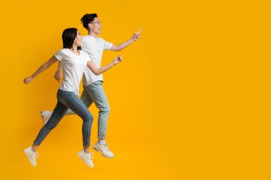 Excited asian couple running towards copy space