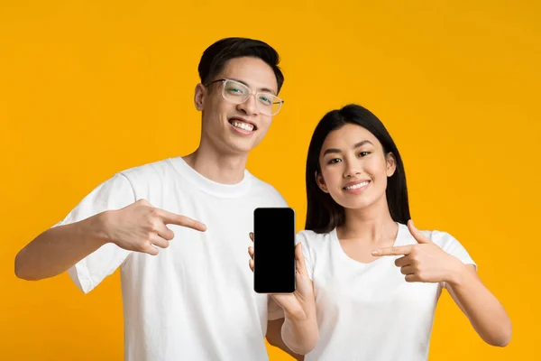 Cheerful asian couple pointing at smartphone with blank screen — 图库照片