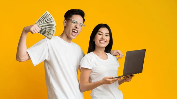Asian man and woman earning online, holding laptop and dollars — Φωτογραφία Αρχείου