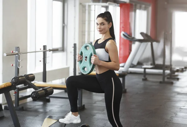 Young woman with barbell weight plate working out in sports club — Stockfoto