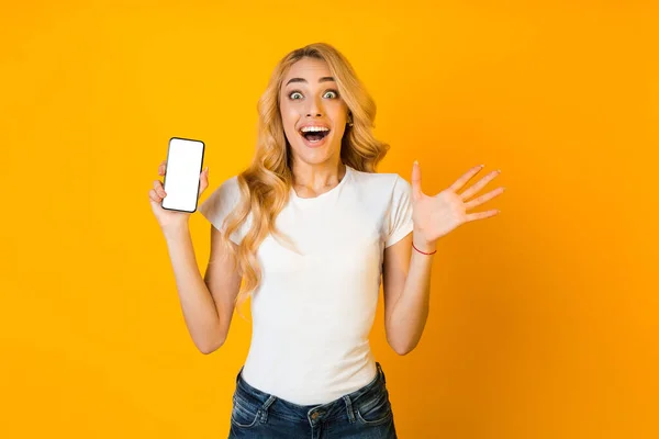 Nueva aplicación impresionante. Chica sorprendida mostrando teléfono con pantalla en blanco — Foto de Stock