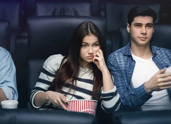 Boring date. Weary young girl with boyfriend watching movie in dark cinema