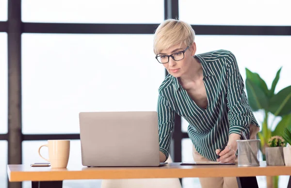 Exitosa dama de negocios usando el ordenador portátil tomando notas de pie en el cargo — Foto de Stock