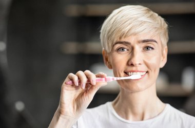 Woman Brushing Teeth Smiling To Camera Standing In Bathroom Indoor