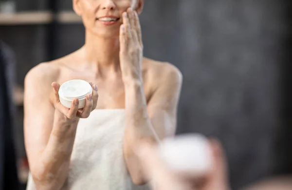 Femme méconnaissable appliquant la crème visage dans la salle de bain à la maison, recadré — Photo