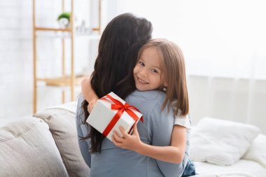 Cute little girl hugging her mom, holding gift box