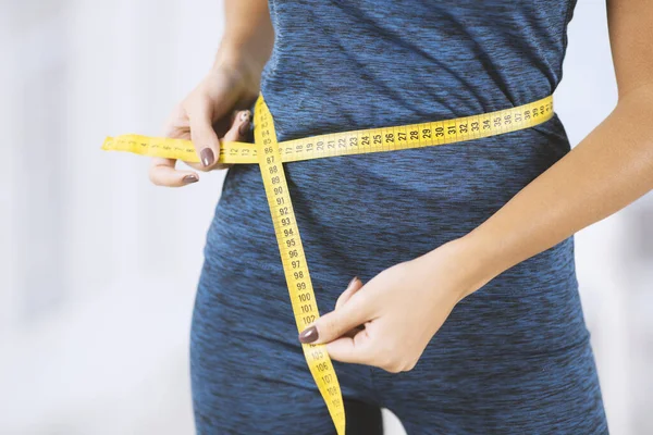 Weight loss concept. Slim woman in sportswear measuring her waist with tape measure indoors, closeup view — Stockfoto