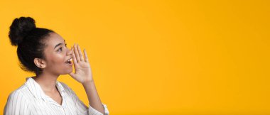 Excited afro woman shouting at copy space with hand near mouth