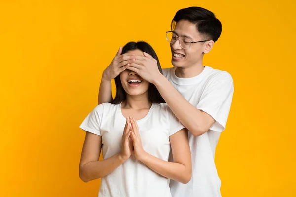 Asian man standing behind his girlfriend and closing her eyes — Zdjęcie stockowe
