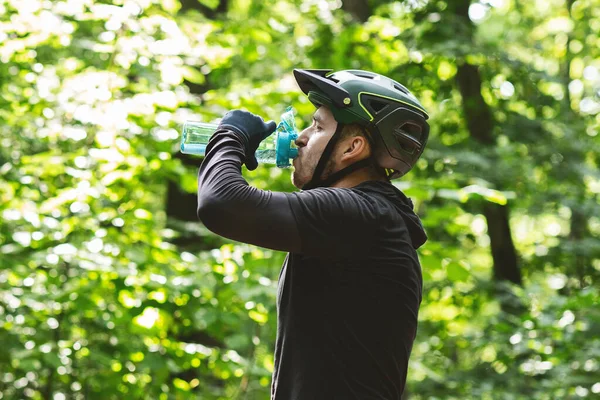 Male cyclist drinking water while riding in forest