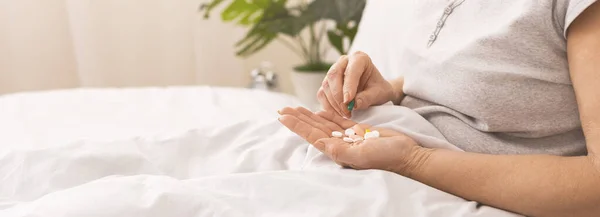 Señora mayor sosteniendo un montón de pastillas en la mano en la cama — Foto de Stock