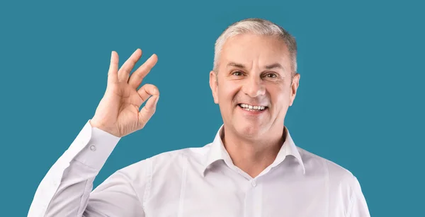 Smiling elderly man gesturing ok sign at blue studio — Stock Fotó