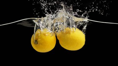 Two tasty lemons splashing into transparent water on black background, panorama