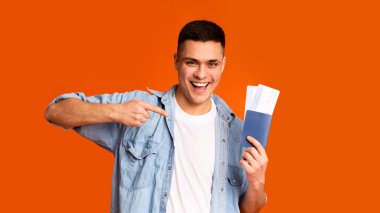 Emotional young man pointing at passport with tickets