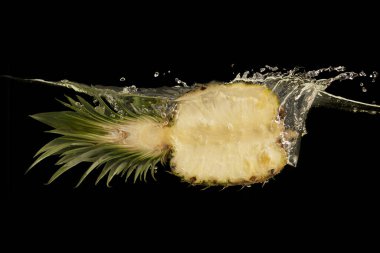 Half of juicy pineapple falling into transparent water on black background