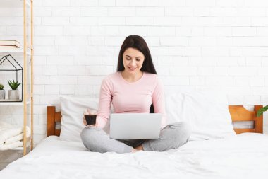 Young woman working on laptop, sitting on bed