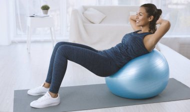 Sporty Latin woman doing abs exercises on fitness ball at home