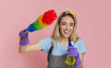 Smiling girl holds colorful duster brush and threatens with spray