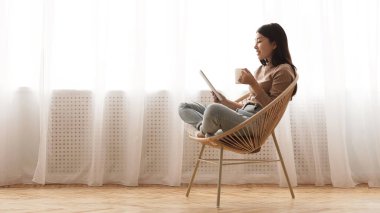 Free time. Girl using tablet and drinking coffee in wicker chair
