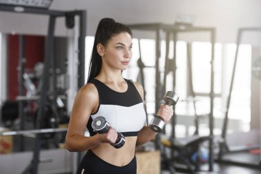 Sports training. Young woman with dumbbells working out in gym