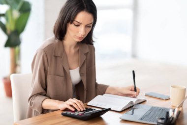 Portrait of manager using calculator and writing in notebook