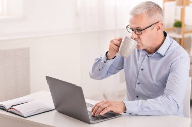 Happy senior man using laptop and drinking coffee