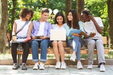College Students With Laptop Preparing For Lessons On Bench In Campus