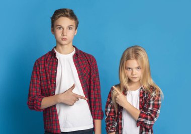 Siblings pointing at each other, accusing and blaming on blue background