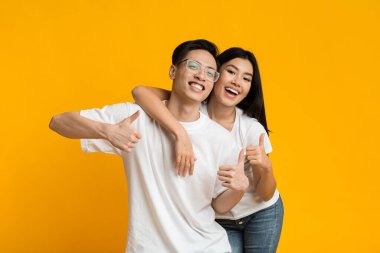 Joyful asian man and woman hugging and showing thumbs up