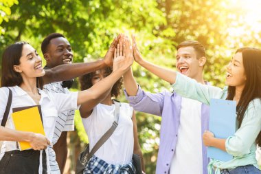 Happy international college students joining their hands together, celebrating success outdoors