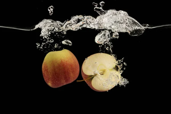 Halves of red apple flowing into clear water with splash on black background — 스톡 사진