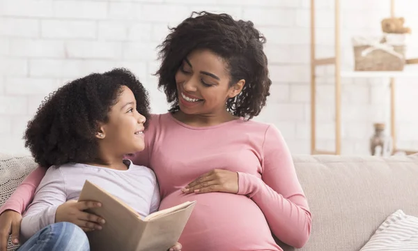 Маленька чорна дівчинка і її вагітна мама насолоджуються читанням книги разом — стокове фото