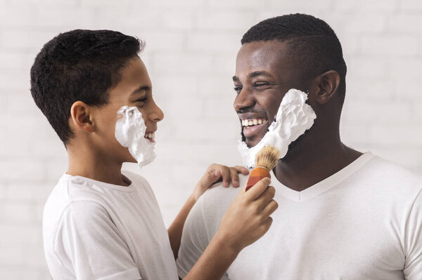 Little Black Son Using Shaving Brush Applying Foam To Fathers Face