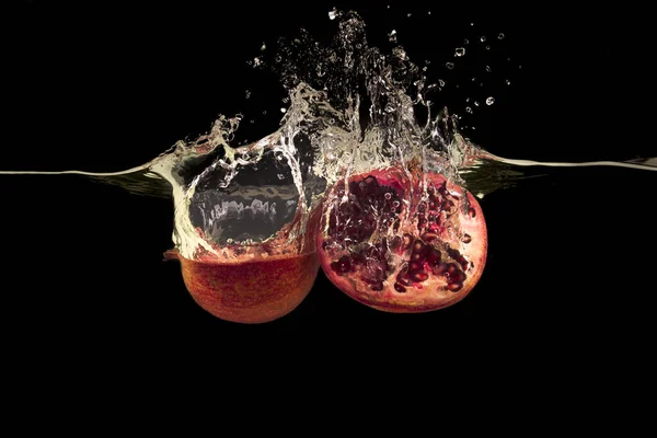 Delicious pomegranate halves and splashing water on black background — 스톡 사진