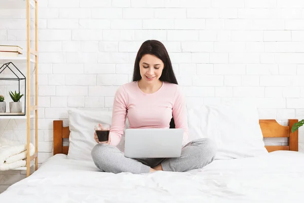 Молодая женщина работает на ноутбуке, сидит на кровати — стоковое фото