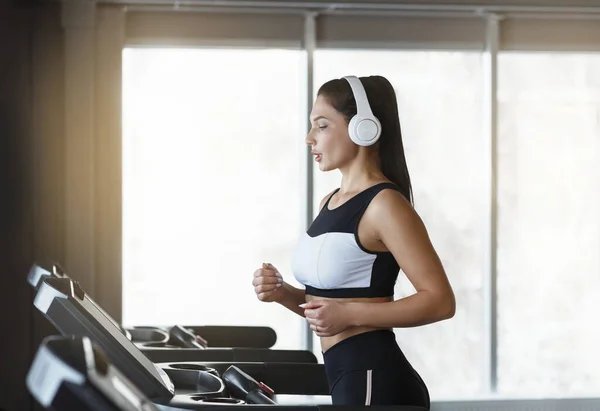 Mulher bonita com fones de ouvido ouvindo música enquanto corria em esteira no ginásio — Fotografia de Stock