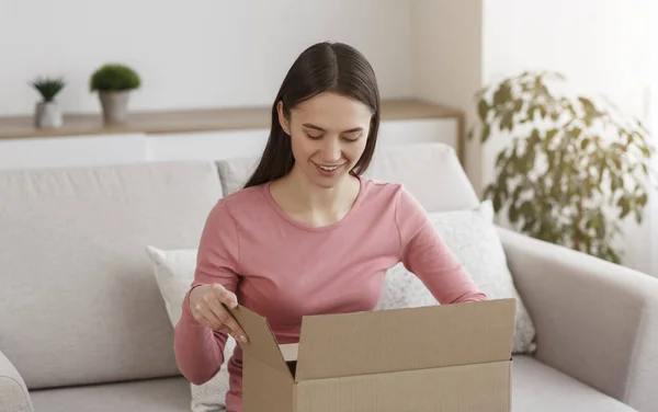 Young smiling girl unboxing cardboard parcel at home — Stockfoto