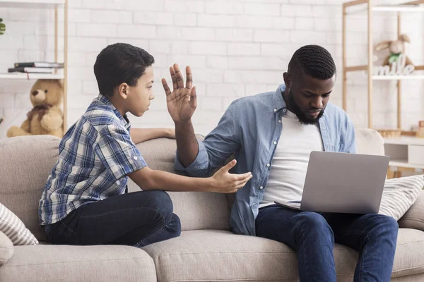 Pequeño afro hijo pidiendo atención de su padre ocupado con el ordenador portátil — Foto de Stock